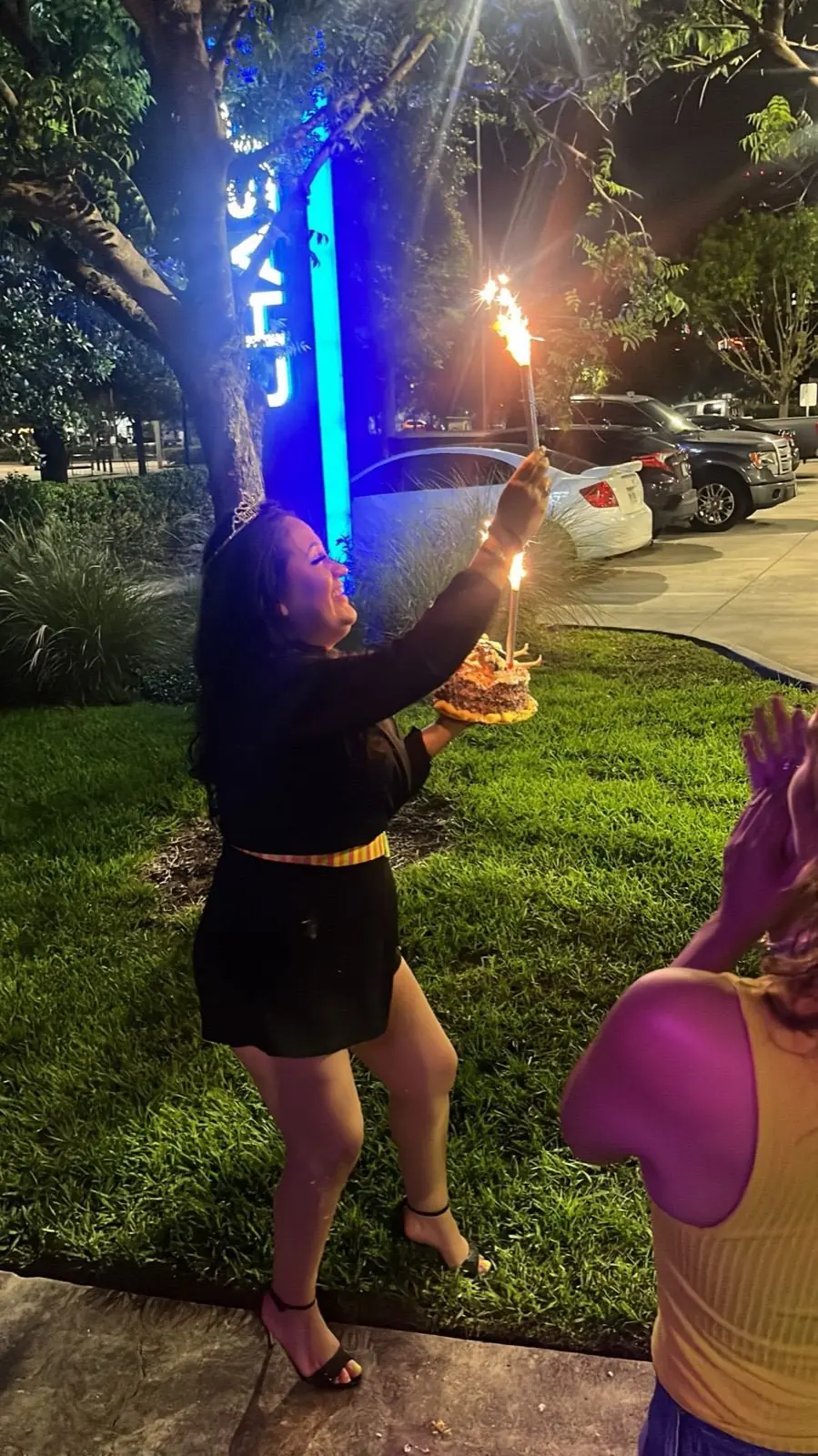 A rider holding a sparkler-topped cake beside the bike at night