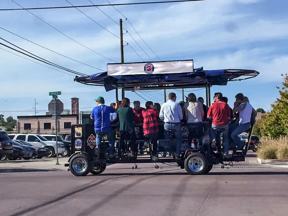 A full group riding the bike bar down a Houston street in daylight
