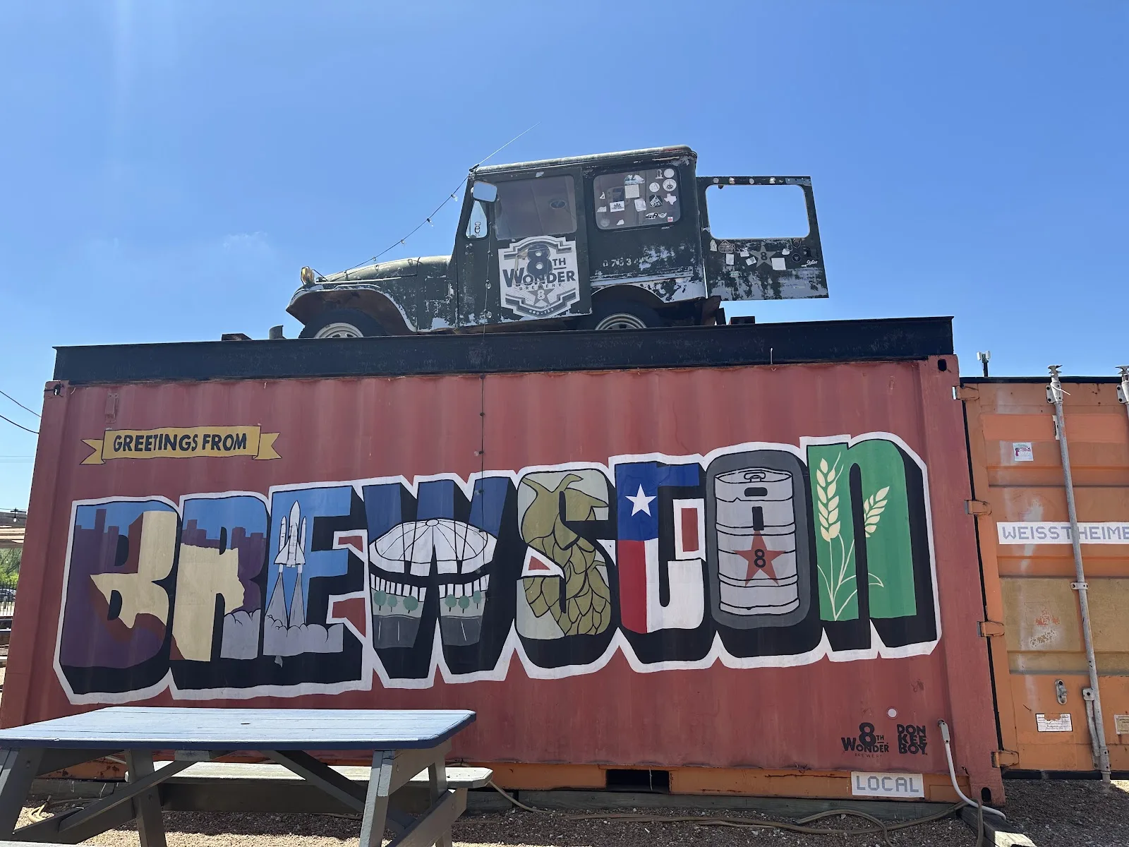 A shipping container painted with a Greetings from Brewston mural in the 8th Wonder Brewery backyard