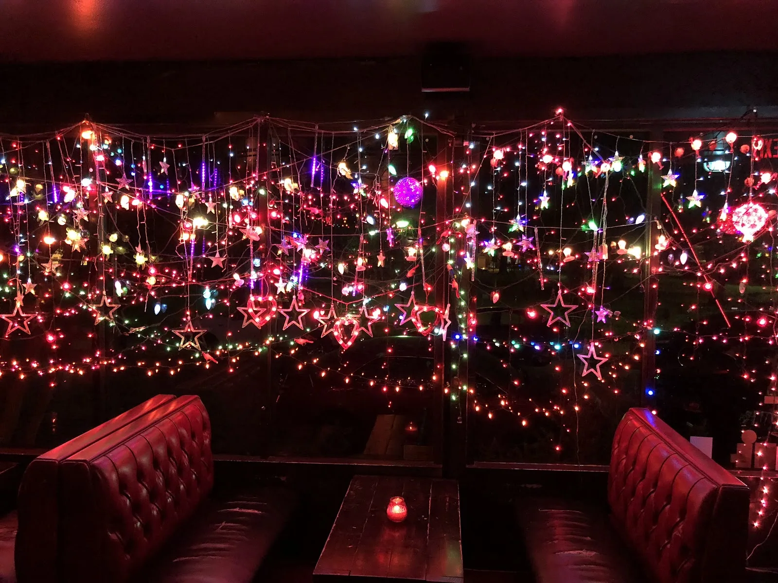 Red leather booths under strings of colored lights in the front window at Grand Prize Bar