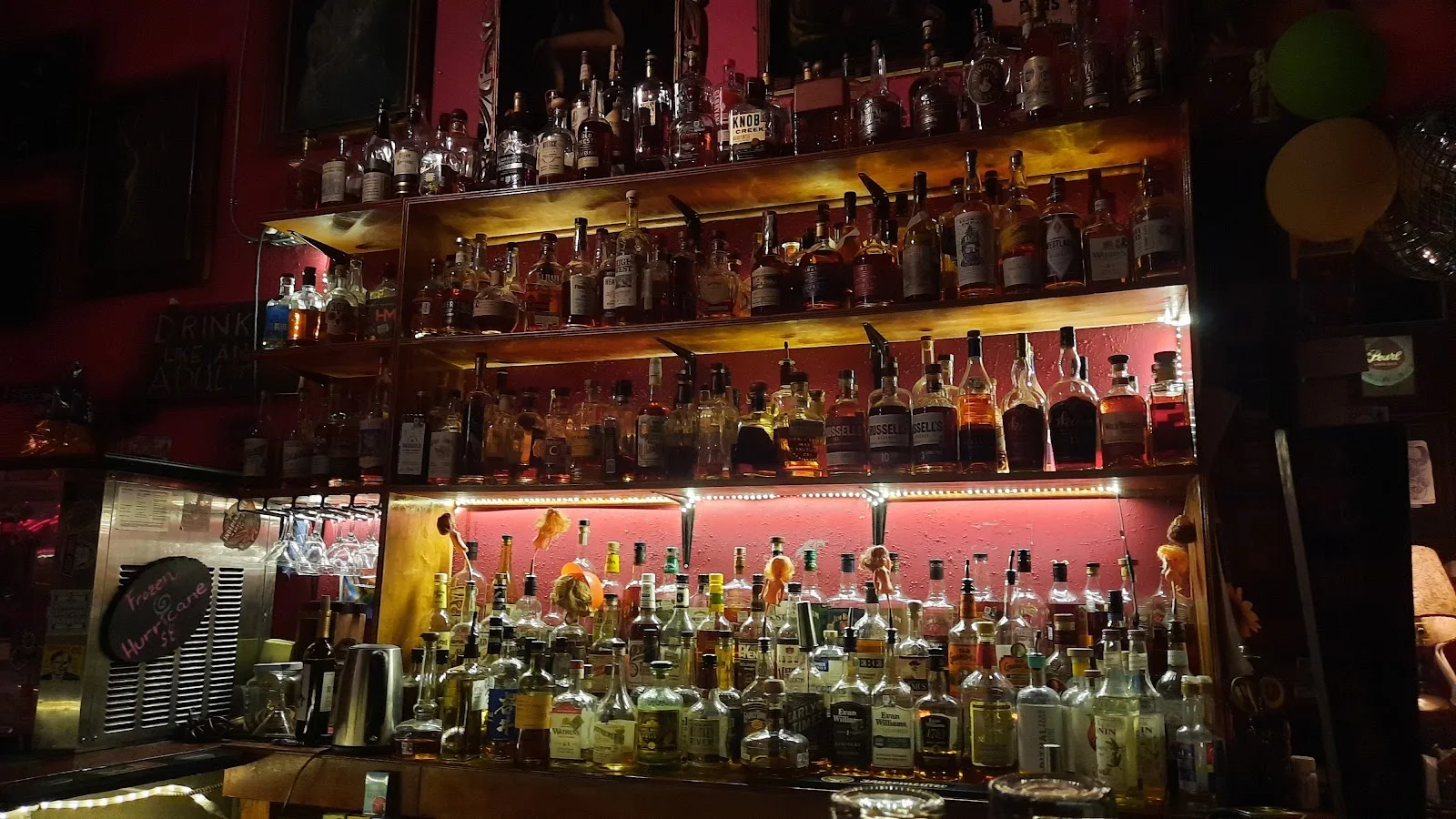 Shelves of bourbon and rye under red light at Poison Girl on Westheimer