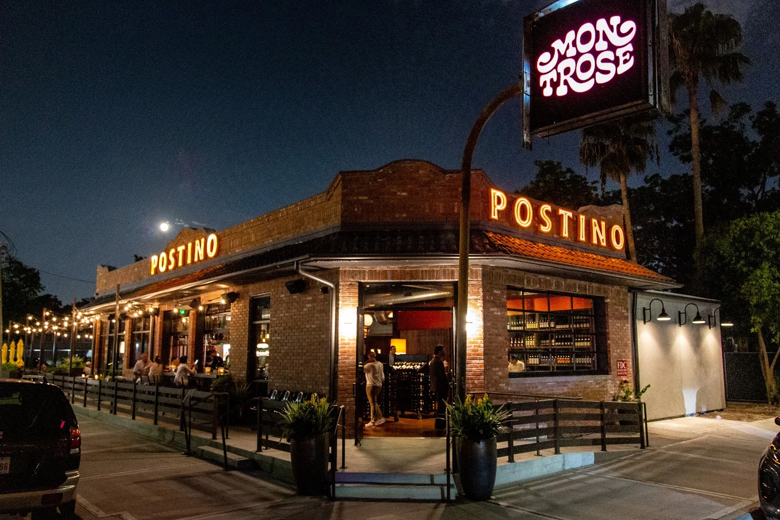 The corner patio of Postino on Pacific Street at night, under the neon Montrose sign
