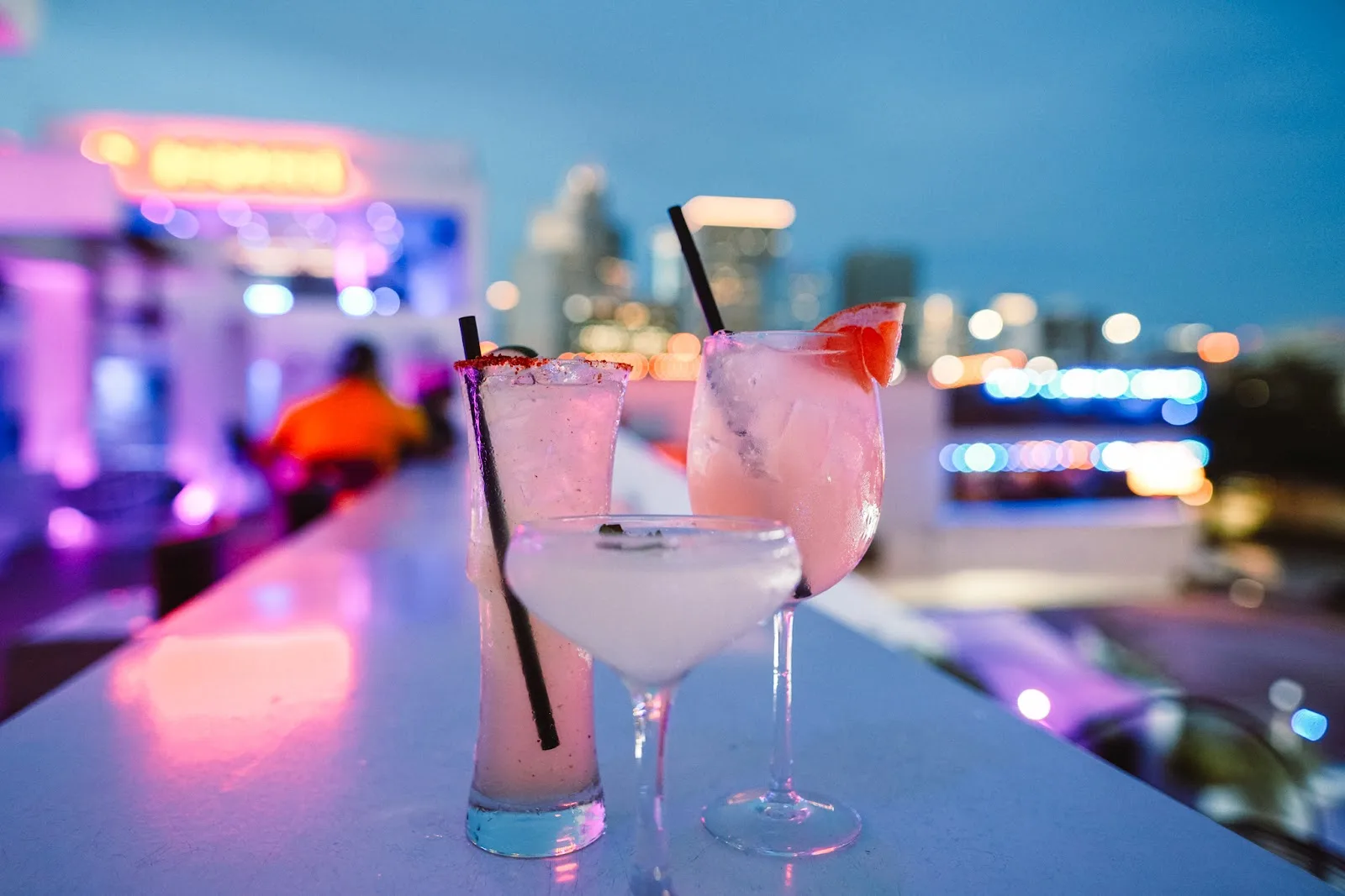 Three cocktails on the rooftop bar at 77 Degrees with downtown Houston lit up behind them