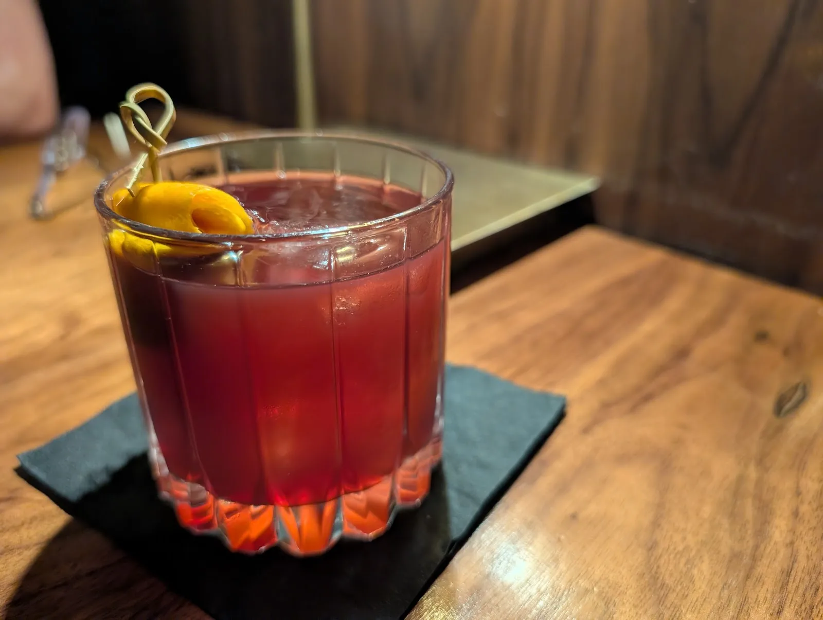 A red cocktail with a citrus twist on the wooden bar at Jethro&rsquo;s in Midtown Houston