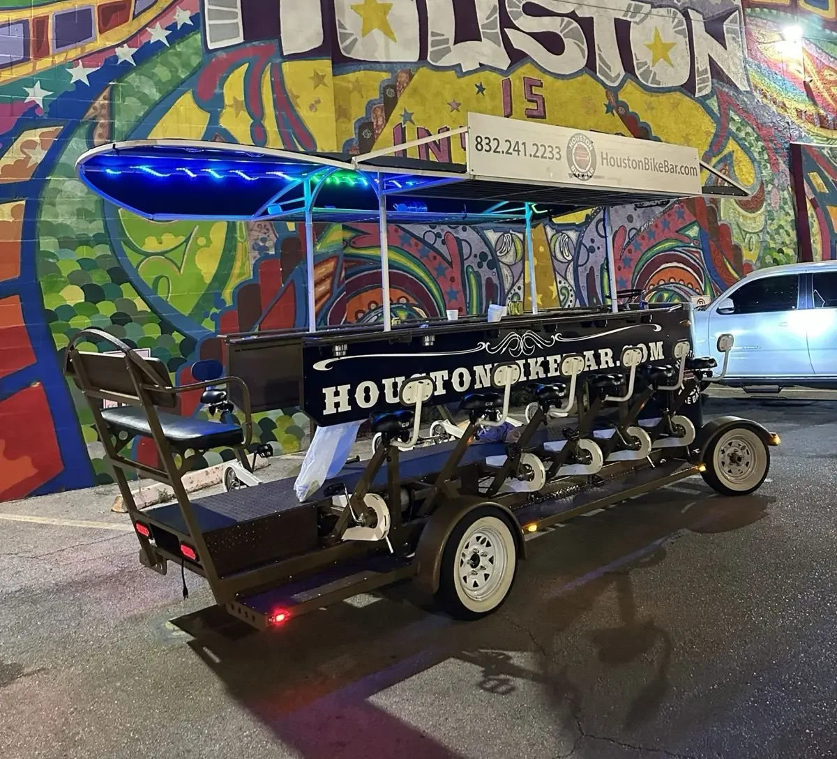 A sixteen-seat party bike parked under a Houston mural at night