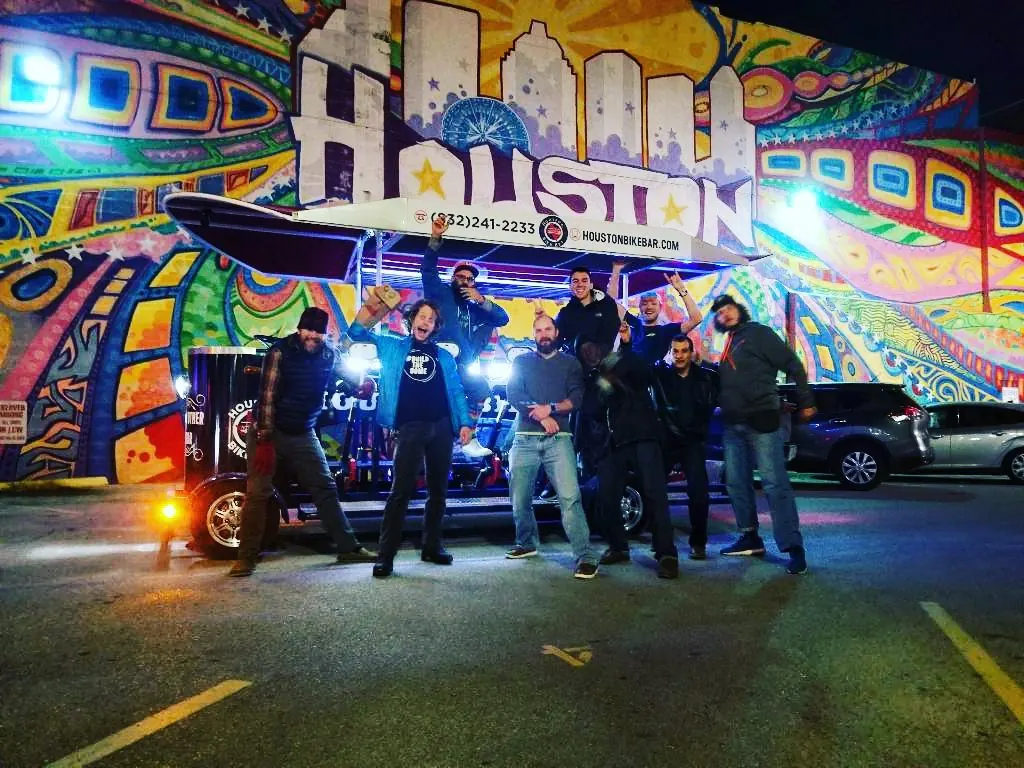 A group posed with the Houston Bike Bar in front of a mural at night